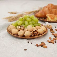 Набор круглых деревянных тарелок с виноградом и грецкими орехами на светлой скатерти