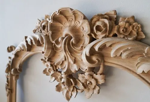 Изящная деревянная рама с детализированной резьбой в виде цветов и листьев.