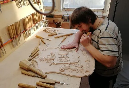 Мастер вручную вырезает геральдический барельеф из дерева, используя резцы в мастерской STAVROS.