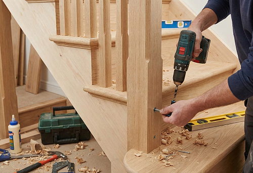 How to attach balusters to steps: a craftsman secures the post on a wooden staircase with a screwdriver, with shavings and markings on the steps.