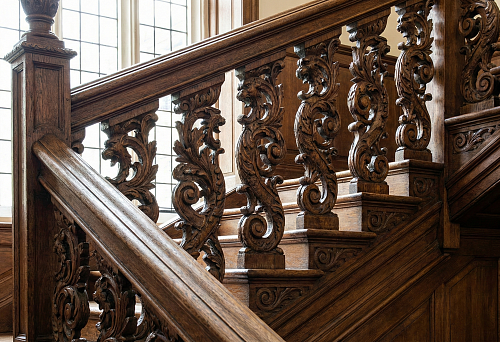 Carved wooden balusters on a classic staircase: intricate ornament with curls, dark wood shade, massive handrail.