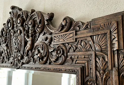 Mirror in a massive hand-carved wooden frame: Baroque ornament, angels and Art Deco geometric motifs, dark patina