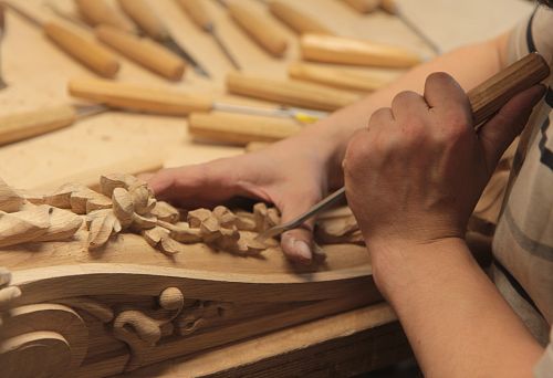 The craftsman carves decorative relief on a wooden wall panel