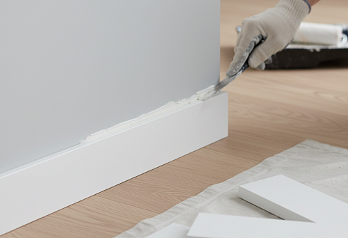 Installation of white polystyrene skirting board for painting using a spatula in a modern interior