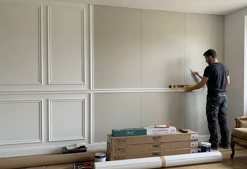 Boiserie installation: the master glues polyurethane molding onto wall panels, leveling it