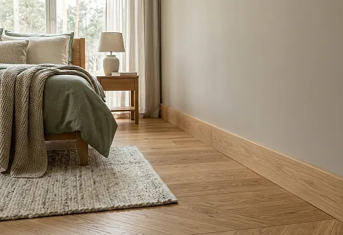 Wooden baseboard in the bedroom: high profile matching the parquet tone against a light wall and soft textiles