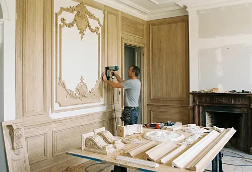 The master installs decorative overlays and moldings on a wall panel in a classic interior