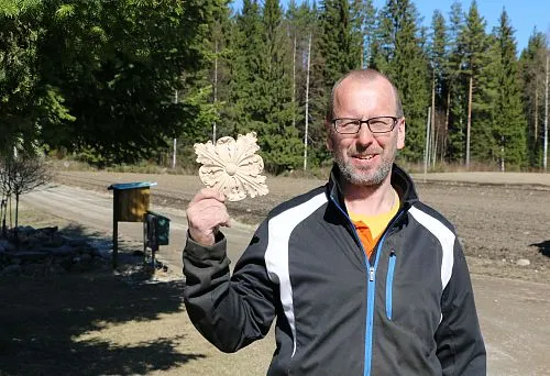 A man on the street holds carved wooden furniture decor against a forest backdrop