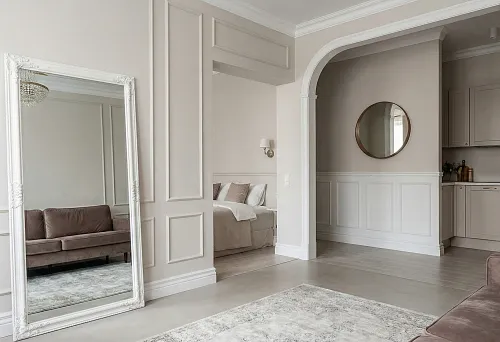 Studio apartment with decor zoning: wall moldings, high white baseboard and large framed mirror separate zones