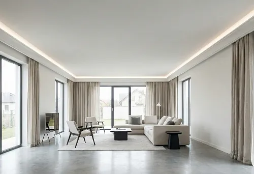 Modern living room with ceiling perimeter and hidden lighting: smooth ceiling, light line along the contour, large windows and neutral furniture.
