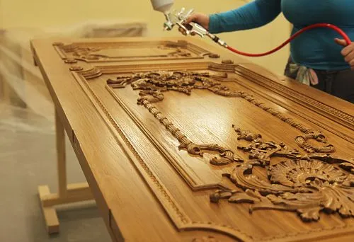 Process of applying oil to a wooden panel with intricate carved ornament.
