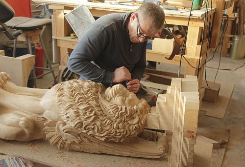 Wooden lion sculpture in the process of being worked on by a craftsman.