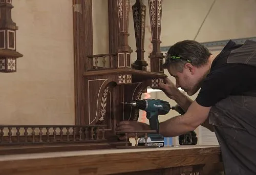 A craftsman working on carved furniture made of natural wood, using power tools
