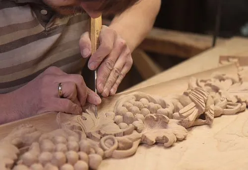 The craftsman manually carves a decorative wooden element with grapevine &mdash; the process of creating architectural framing