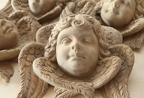 Carved angel head sculpture with wings, handcrafted from oak, with detailed rendering of the face and feathers.