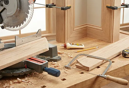 Cutting wooden skirting board and architrave on a workbench: precise trimming of corners and joints using a saw, clamps, and hand tools without creating gaps