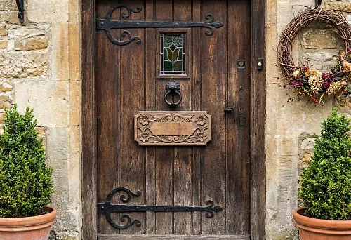 Decorating a Wooden Door with a Carved Overlay: Decorative Panel on the Door Leaf, Forged Hinges, and Stone Facade