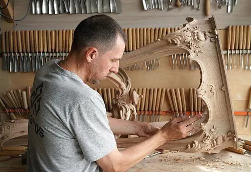 Craftsman manually works with carved solid wood furniture element.