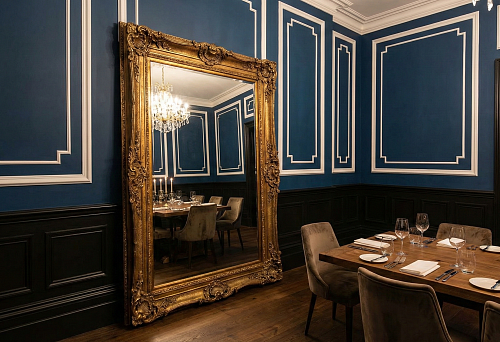 Dining room with dark high baseboard and wall panels, blue walls with large moldings, and a large mirror in a gold frame