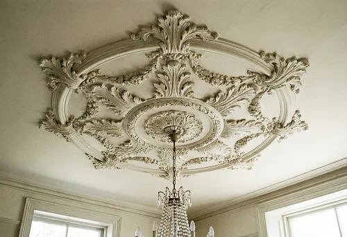 Ceiling stucco rosette with a relief ornament around the chandelier in a classic interior