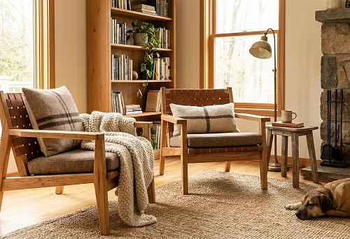 Reading nook: two solid wood armchairs by the window, a blanket and pillows in a cozy living room