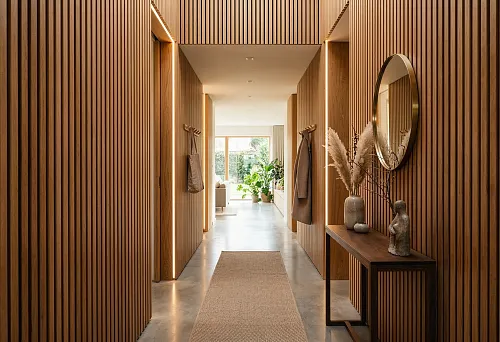 Slat panels in the hallway with warm lighting, a console, and a round mirror