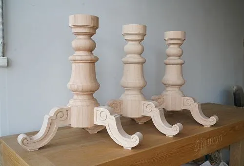 Three wooden coffee table bases with classic design and heavy carved legs on a carpenter's workbench