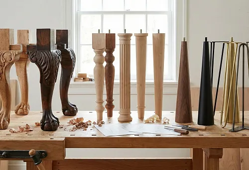 Carved wooden table legs in the shape of paws with ornamentation, installed on a workbench in a workshop.