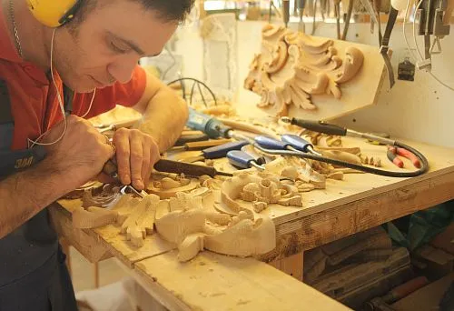 The craftsman manually carves a decorative element from solid wood
