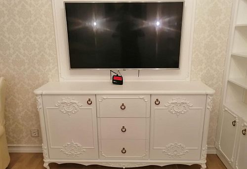 White chest of drawers with carved fronts and bronze hardware, mounted under the TV on the wall