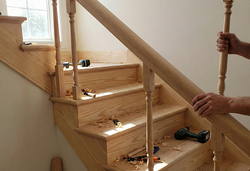 Installing balusters on a wooden staircase: the craftsman fits the post and checks the fit before fastening