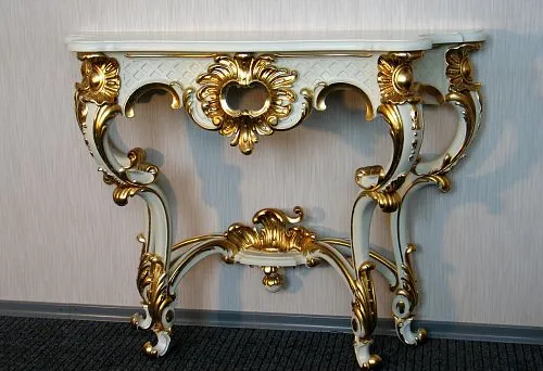 Luxurious console table base with hand-carved details and gold ornamentation in classic style against a light wall