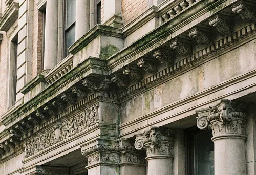 Building facade with architectural stucco: cornices, capitals and decorative frieze on stone cladding, an example of durable facade decor.