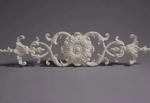 Classic molding decoration element with central rosette and symmetrical scrolls, executed in light tone on gray background.