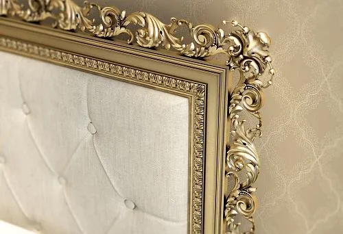 Luxurious wooden bed with carved golden decor on the headboard, styled in classic design against elegant wallpaper.