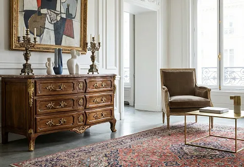 Classic style furniture design: wooden chest of drawers with gilded hardware, armchair and modern coffee table on a rug in a light living room