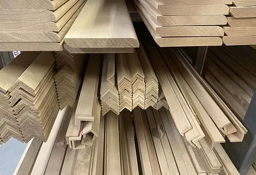 Long wooden poles, angles, and profiled blanks about two meters long, arranged in rows on the warehouse floor