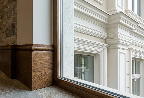 Solid wood baseboard at the panoramic window in the interior and polyurethane facade decor outside