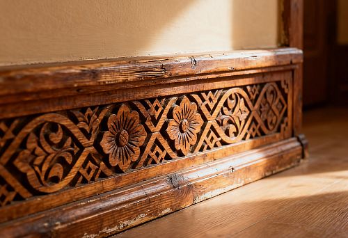 Carved wooden baseboard with Russian-style ornament against a warm natural wood floor