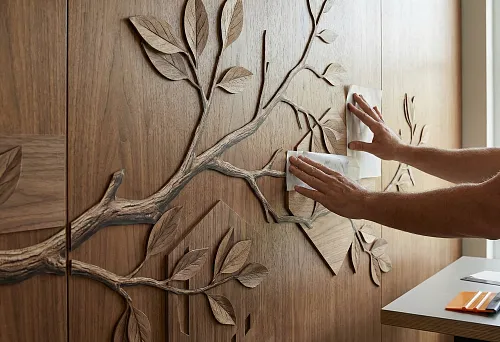 Transferring an interior 3D sticker onto a wooden panel: the master rolls out the relief decor with branches and leaves through mounting film