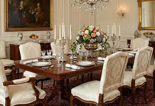 Classic style dining room with upholstered chairs, set table, candelabras with candles, floral arrangement, and crystal chandelier