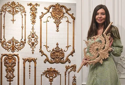 Woman in a salon holding a large carved wooden element with a floral pattern