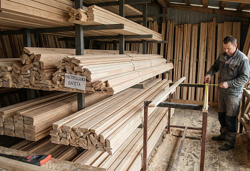 Wooden molding by the meter: a warehouse of linear stock with molding profiles and measuring the length of the slat with a tape measure