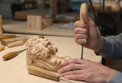 The master's hands using a chisel for wood carving create a detail with an artistic lion's head.