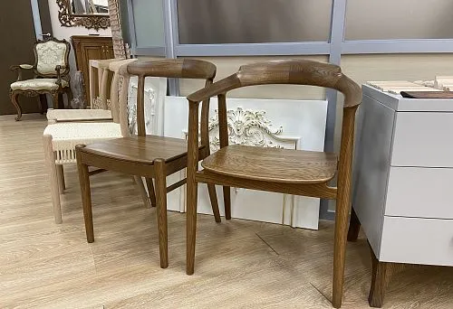 Wooden chairs in unfinished and stained forms, standing side by side in the interior of a furniture showroom