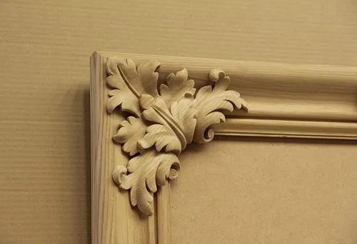 Corner piece of an unfinished carved wooden frame with a decorative oak leaf pattern on a kraft paper background.
