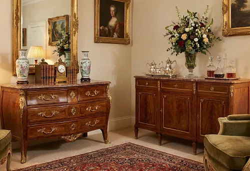 Chest of drawers and cabinet in classic style with gilding, mirror in carved frame, table lamps, porcelain vases and bouquet in the living room