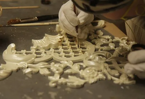 Process of handcrafting a carved decorative element with gold leaf.