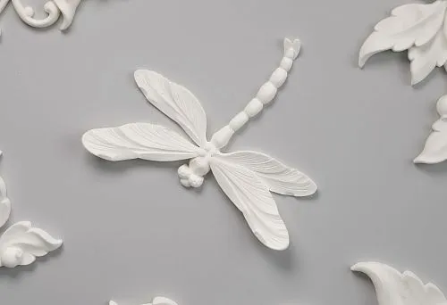 Decorative polyurethane ceiling molding: relief dragonfly, floral ornaments, elegant leaves and flowers on a light gray background.