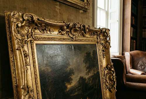 Gilded carved frame with Baroque ornaments and patina in a classic library interior.